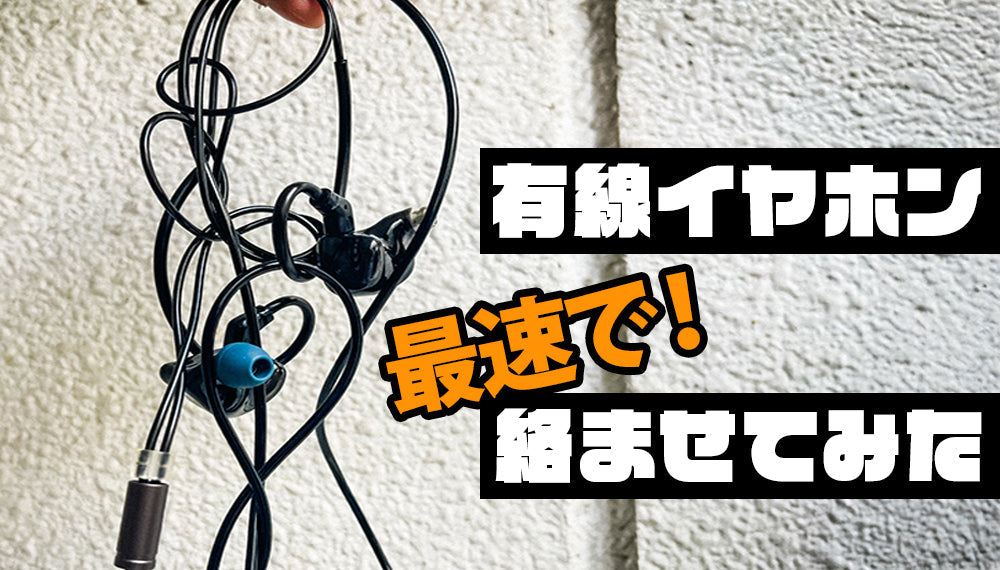 有線イヤホンのコードがひどく絡まっている様子を写したクローズアップ写真。黒いケーブルが無秩序に絡まり合い、片方のイヤホンからは青いイヤーチップが見える。右側には、「有線イヤホン 最速で！絡ませてみた」と書かれている。