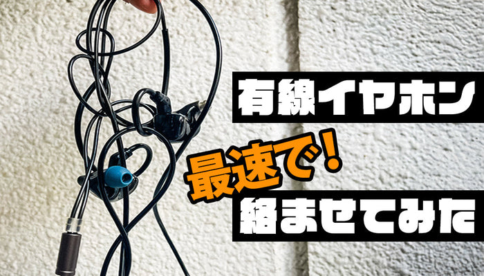 有線イヤホンのコードがひどく絡まっている様子を写したクローズアップ写真。黒いケーブルが無秩序に絡まり合い、片方のイヤホンからは青いイヤーチップが見える。右側には、「有線イヤホン 最速で！絡ませてみた」と書かれている。